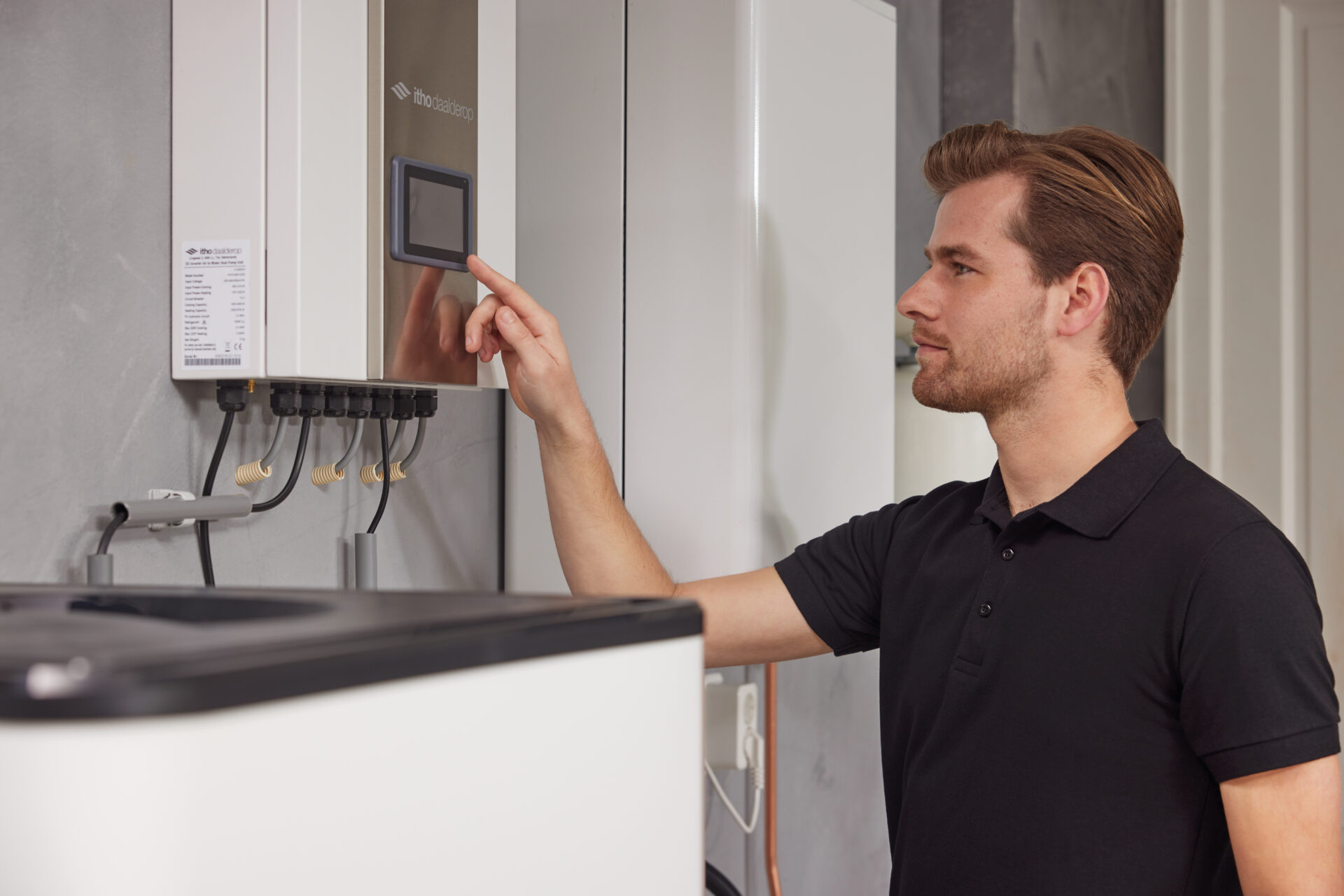 Technicus bedient het touchscreen van een Itho Daalderop Amber Intergas regelmodule van een warmtepomp, wat de gebruiksvriendelijkheid en geavanceerde technologie illustreert.